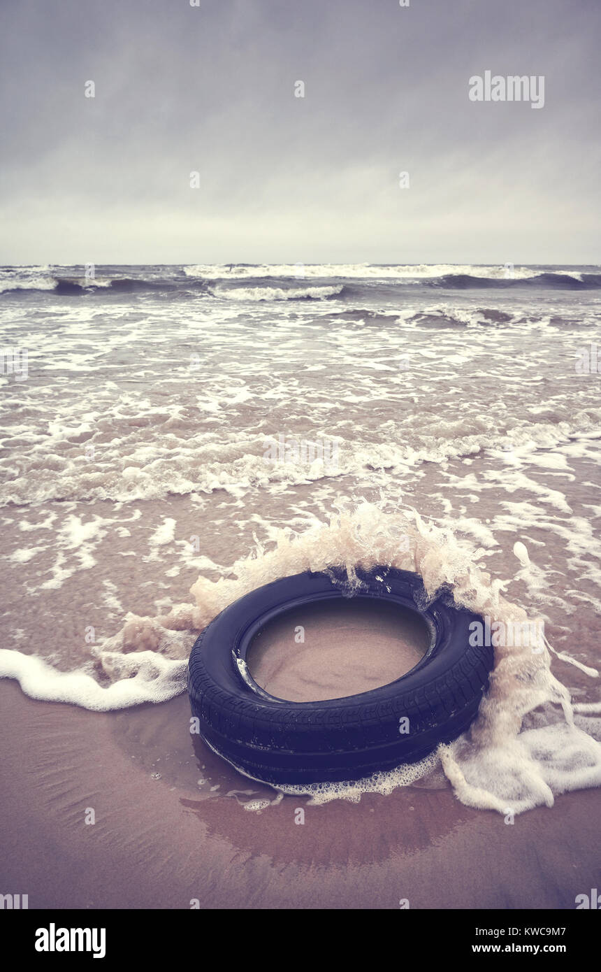 Vieux pneu en caoutchouc noir à gauche sur une plage, la pollution de l'environnement concept, selective focus, photo aux tons de couleur. Banque D'Images