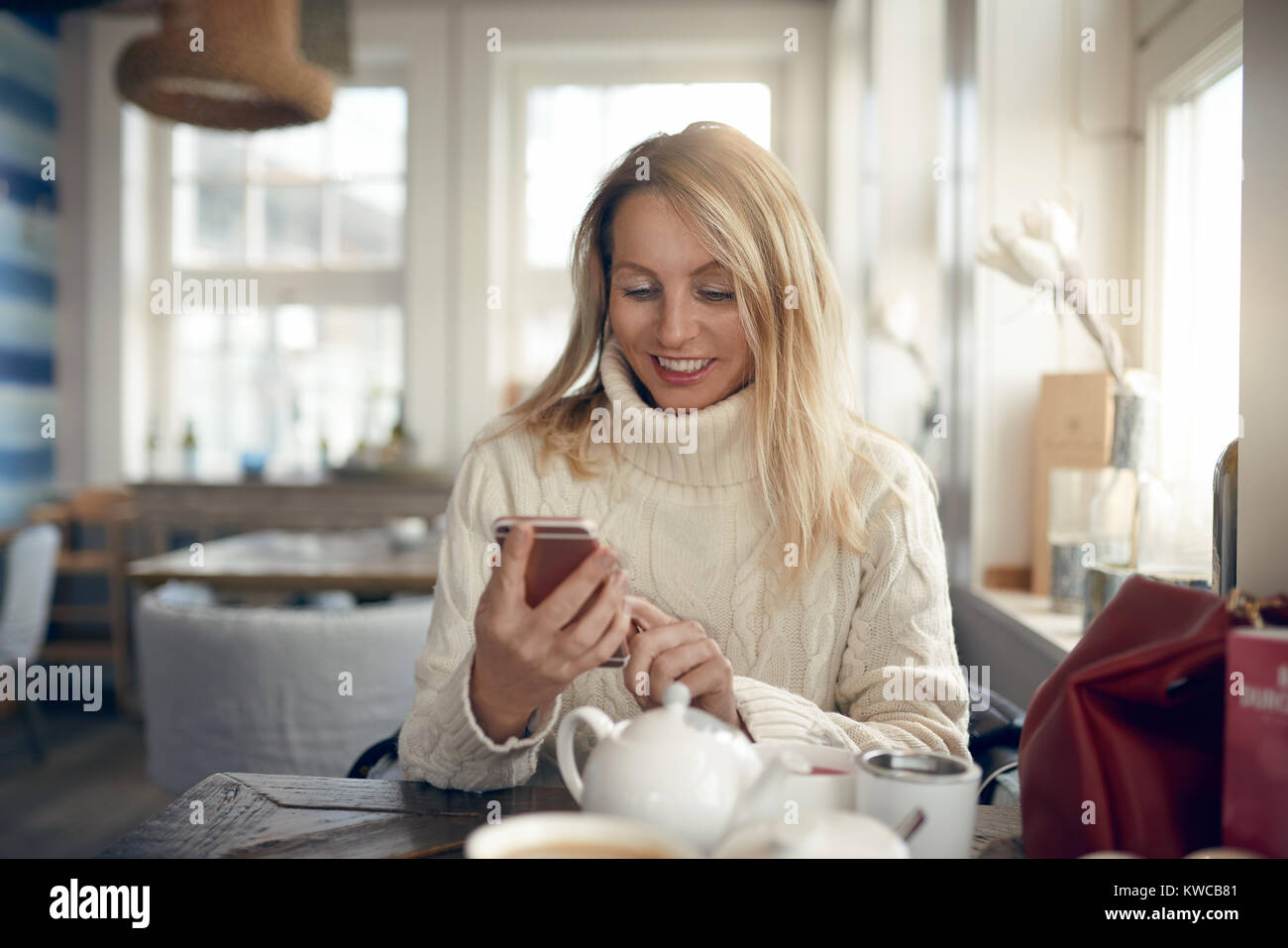 Portrait d'une belle blonde woman smiling lors de la navigation sur internet ou de l'envoi de messages sur le réseau social sur son téléphone portable à la maison Banque D'Images