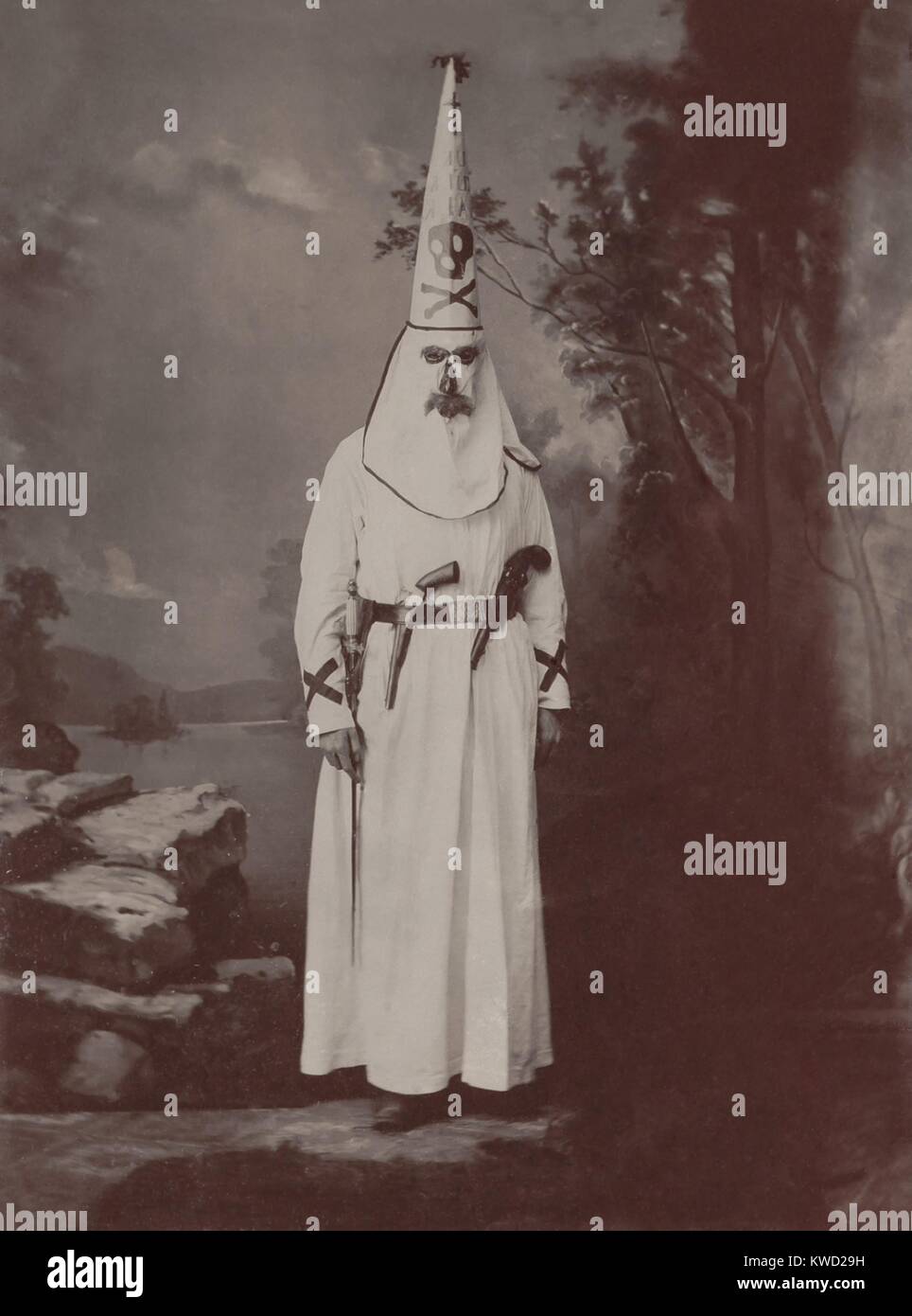 Ku Klux Klansman en robes, armé de deux pistolets et une épée, c. 1880-1905. Photo par Owen A. Kenefick, de Lawrence, Mass. le costume a coloration foncée autour des trous pour les yeux masque, le nez et la bouche, Semblable à Klan costumes illustrent de Harpers Weekly 1868. Le grand, chapeau conique, avec la tête de mort, a été affichée dans la portée dans des tenues Klan Memphis 1872 défilé du Mardi Gras (BSLOC   2017 20 69) Banque D'Images
