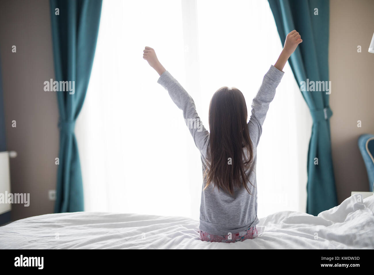 Jolie petite fille s'étire et souriant tout en étant allongé dans le lit le matin Banque D'Images