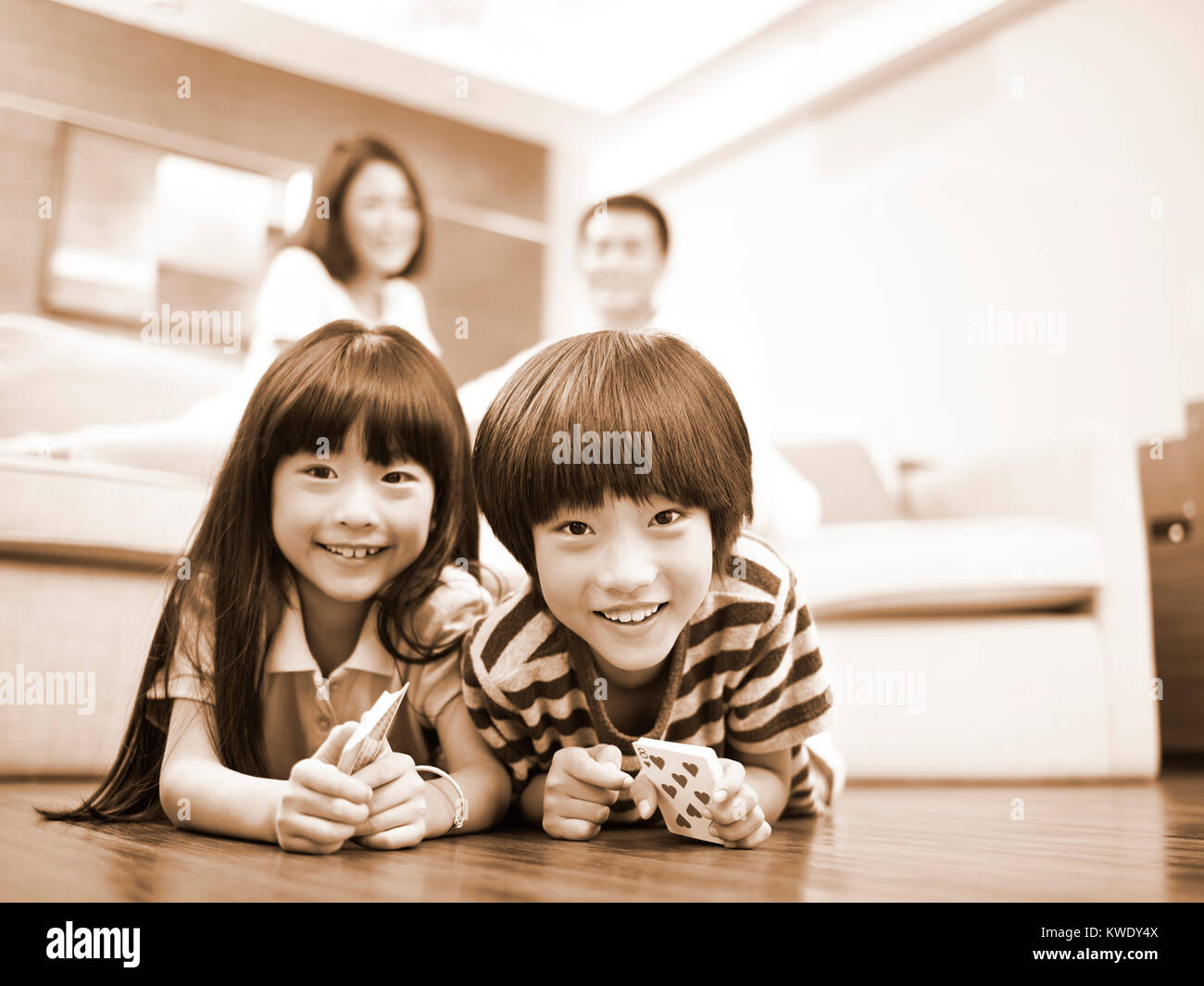 Frère et soeur d'asie se trouvant à l'avant sur le plancher avec les parents dans l'arrière-plan, noir et blanc. Banque D'Images