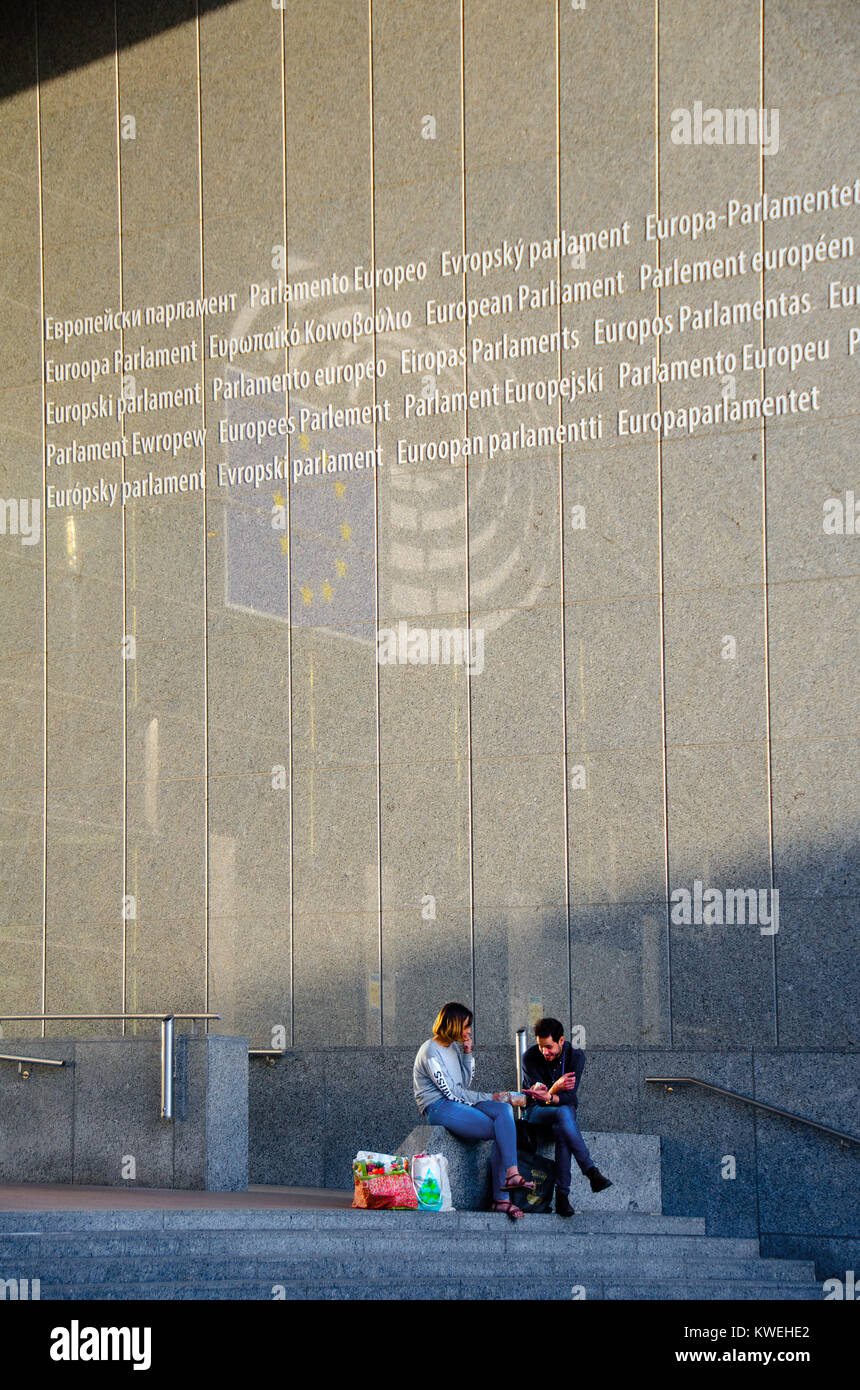 Bruxelles, Belgique. Bâtiment du Parlement européen - l'homme et la femme assis à l'entrée sous multilingual "Parlement européen" Banque D'Images