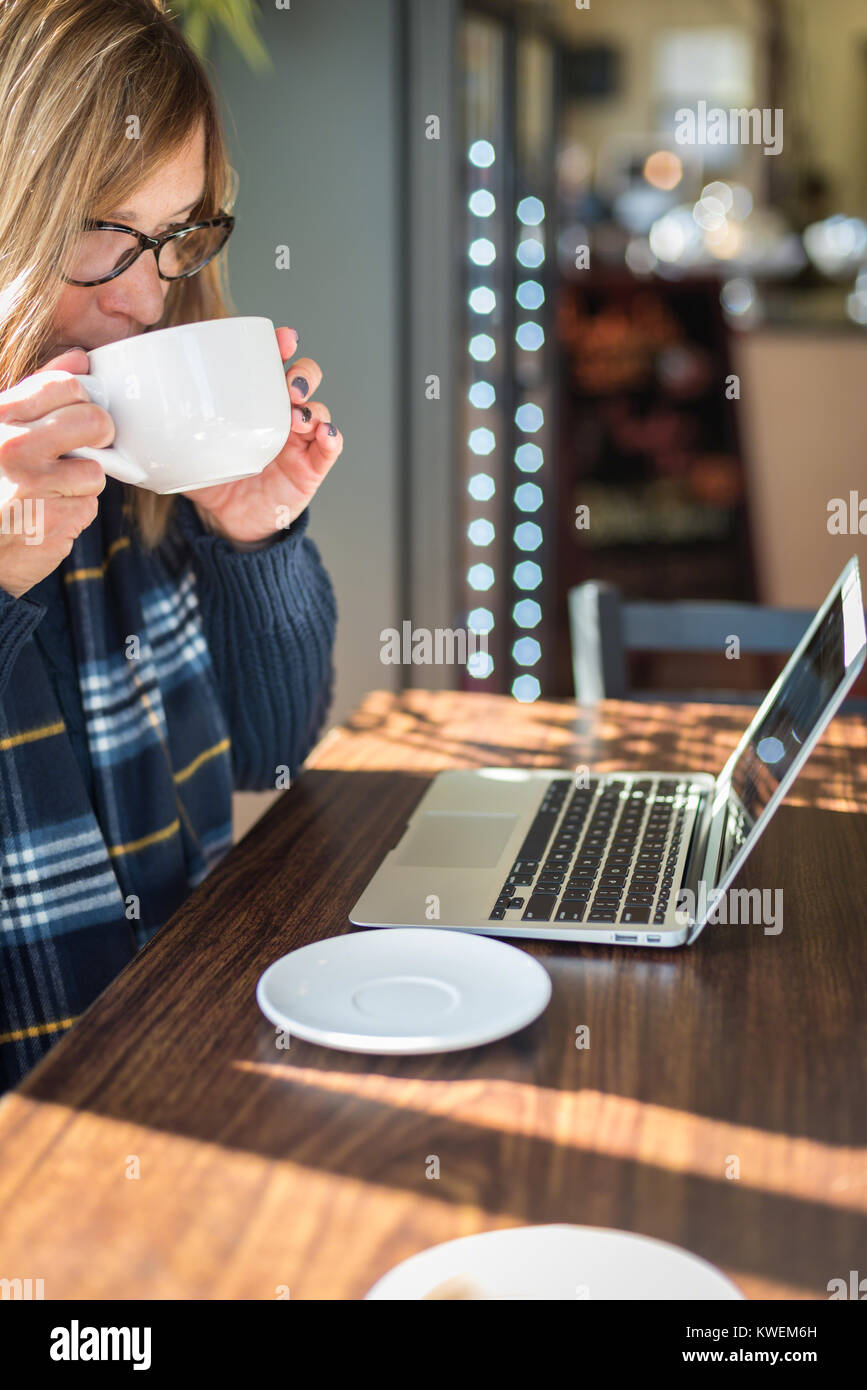 Woman looking at laptop tout en prenant un café au chai sur une journée ensoleillée Banque D'Images