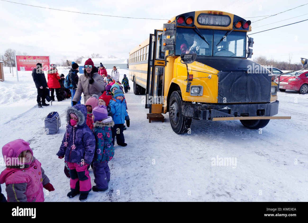 Une file de jeunes enfants de l'école par un bus scolaire à l'hiver au Québec Banque D'Images