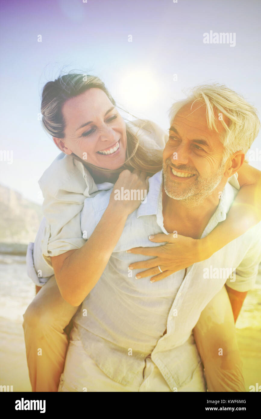 Homme donnant à son épouse souriante un piggy back at the beach Banque D'Images