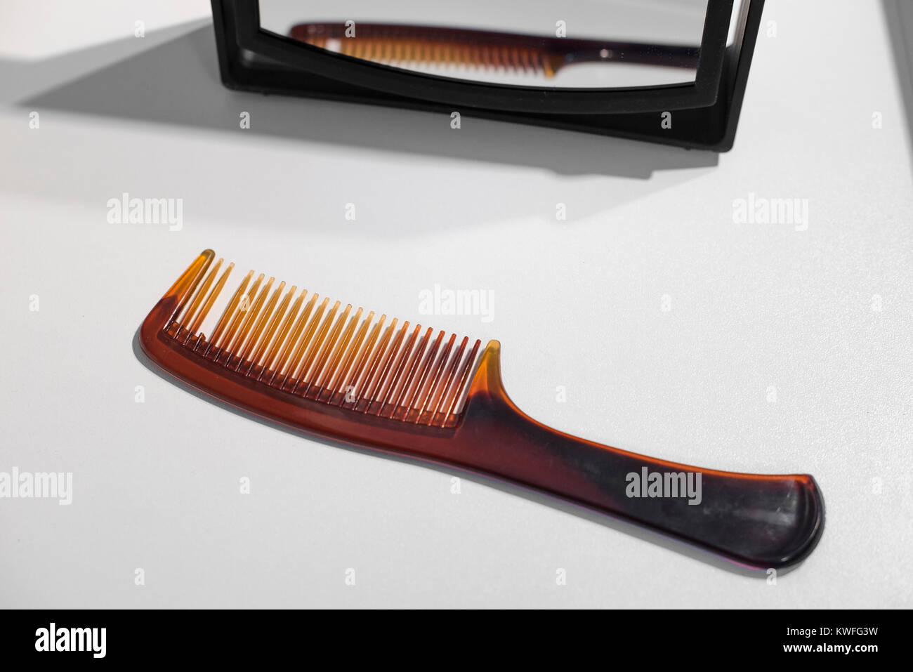Un peigne à cheveux brun avec une dent cassée et un petit miroir à l'arrière-plan Banque D'Images