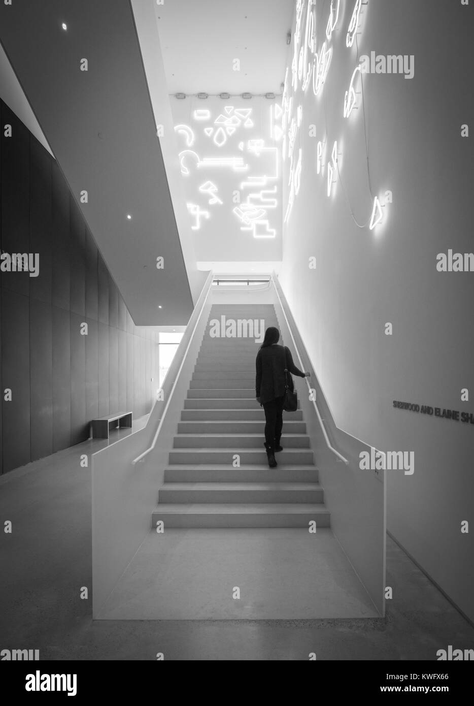 Une jeune femme marche vers le haut des escaliers avec une installation de l'éclairage au néon du nom de Lucky Charms par artiste Pae White à l'Remai Galerie d'Art Moderne. Saskatoon. Banque D'Images