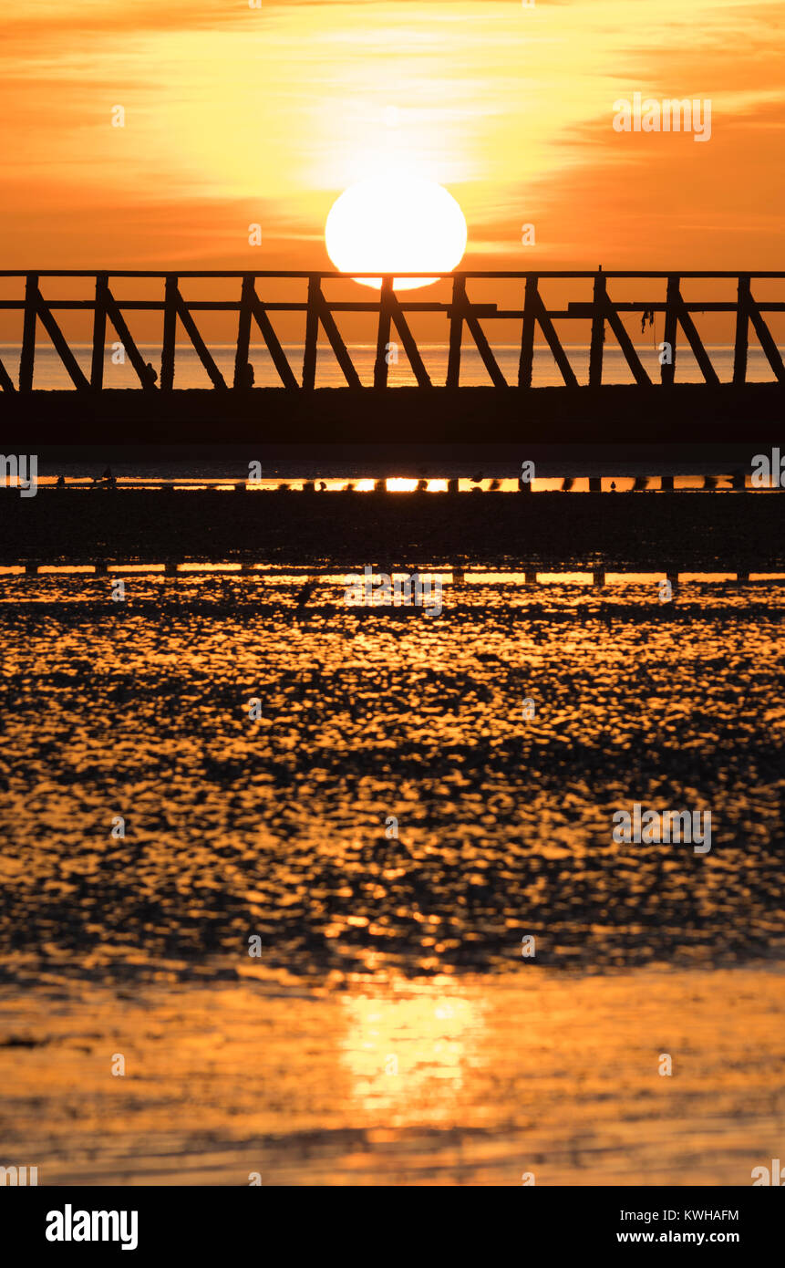 Coucher de soleil sur la plage avec la marée à l'hiver, avec le soleil qui reflète dans le sable humide, au Royaume-Uni. Banque D'Images