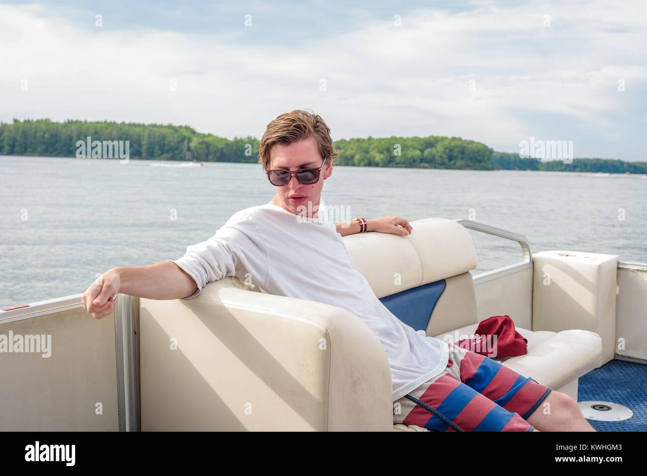 Jeune homme à lunettes assis sur le bateau sur le lac de Banque D'Images