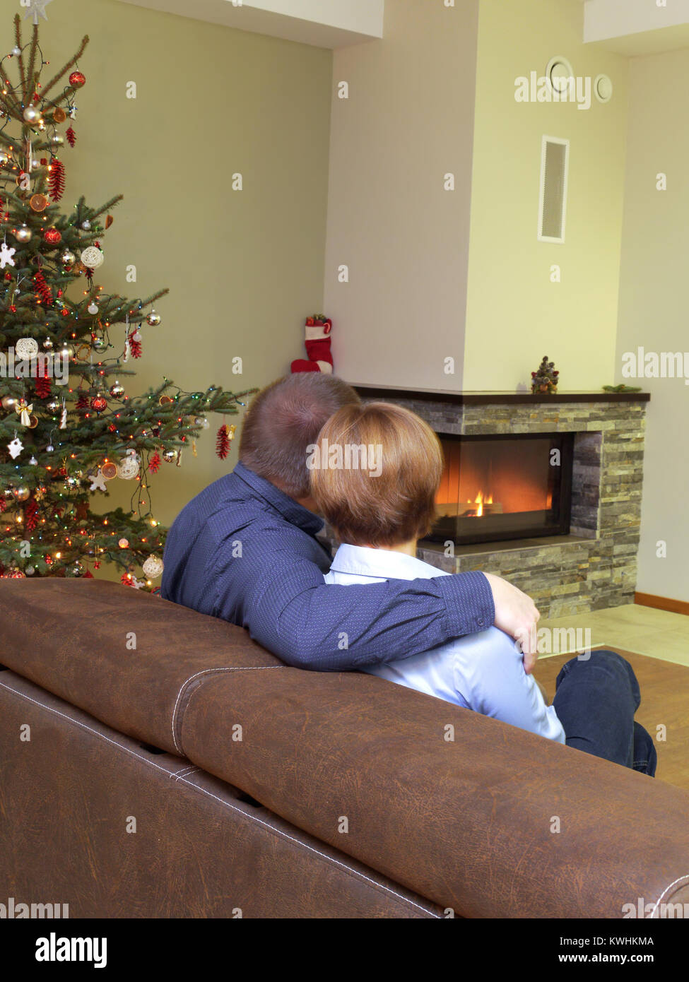 Romantic couple sitting on sofa près de l'arbre de Noël à la cheminée allumée à la Banque D'Images