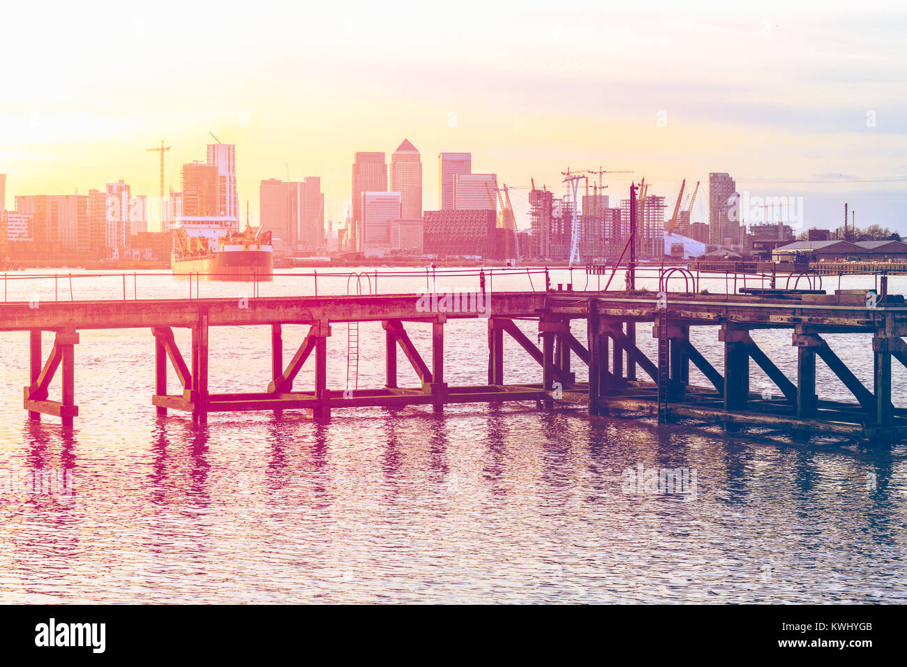 L'ajout d'un coucher de soleil rose sur une jetée désaffectée adjacente à la barrière de la Tamise à Londres avec l'approche d'un navire et de Canary Wharf en arrière-plan Banque D'Images