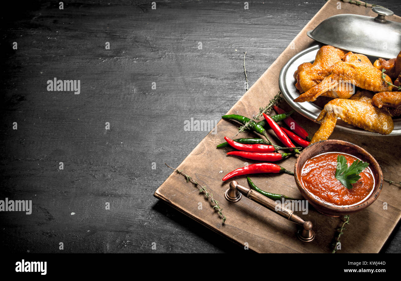 Ailes de poulet avec sauce et Hot Chili Peppers. Sur le tableau noir. Banque D'Images