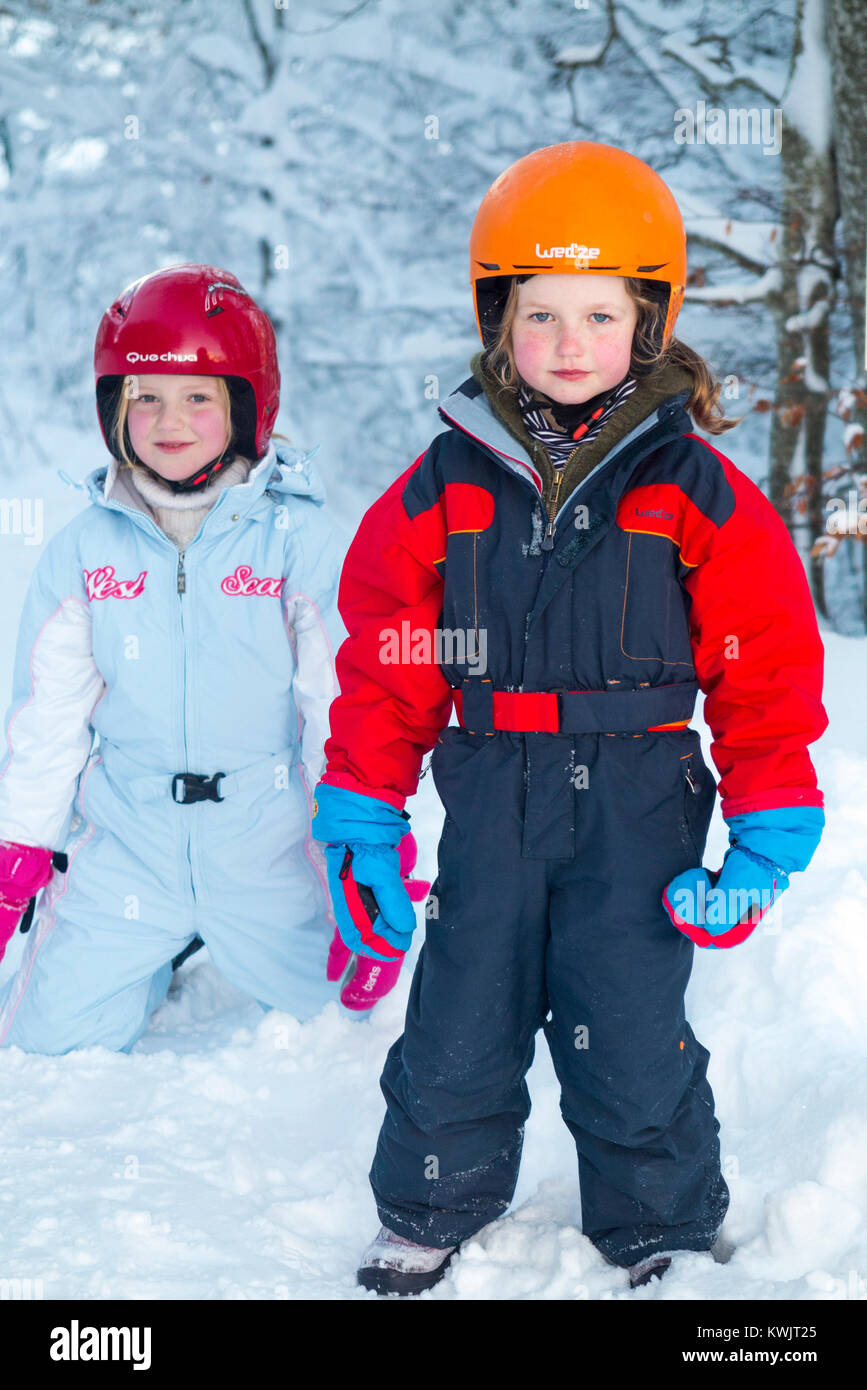 Filles, sœurs, âgés de 5 et 7 ans, et portant des casques de ski freecycle pour la sécurité, profitez de l'hiver la neige dans leur seconde main, élégant & charity shop wear Banque D'Images