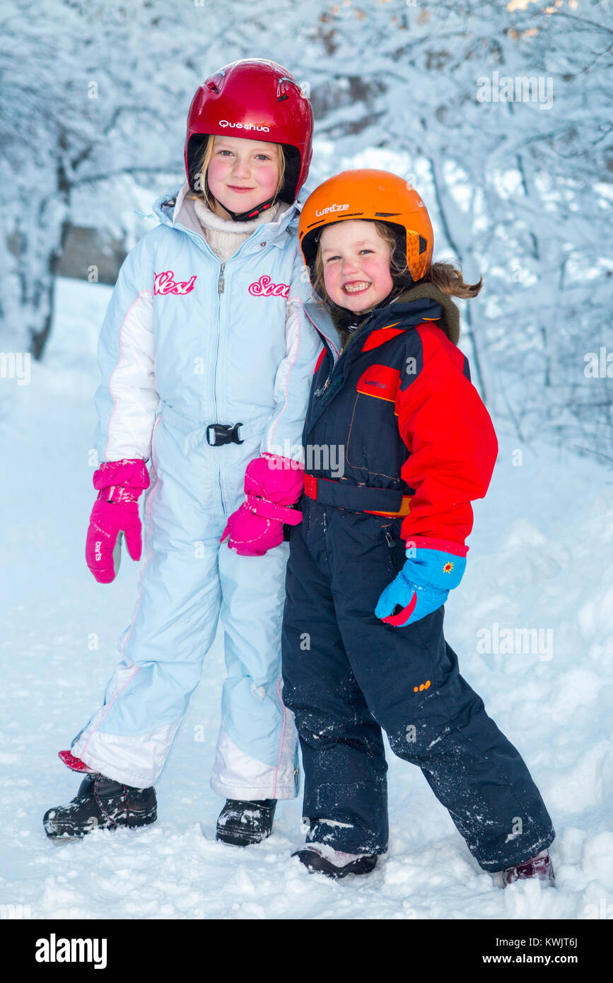 Filles, sœurs, âgés de 5 et 7 ans, et portant des casques de ski freecycle pour la sécurité, profitez de l'hiver la neige dans leur seconde main, élégant & charity shop wear Banque D'Images