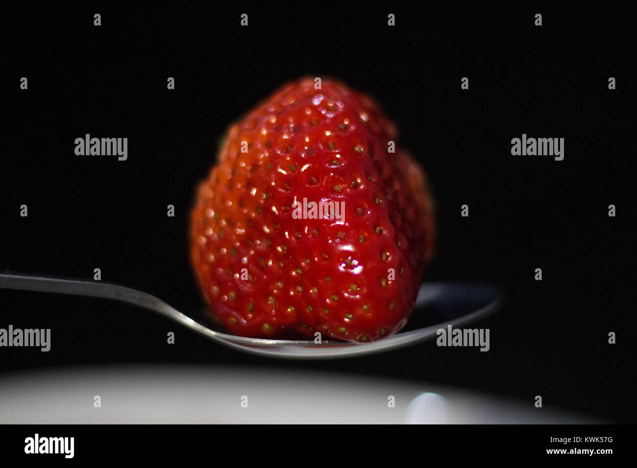 Fraise rouge dans une cuillère en fond noir avec du miel Banque D'Images