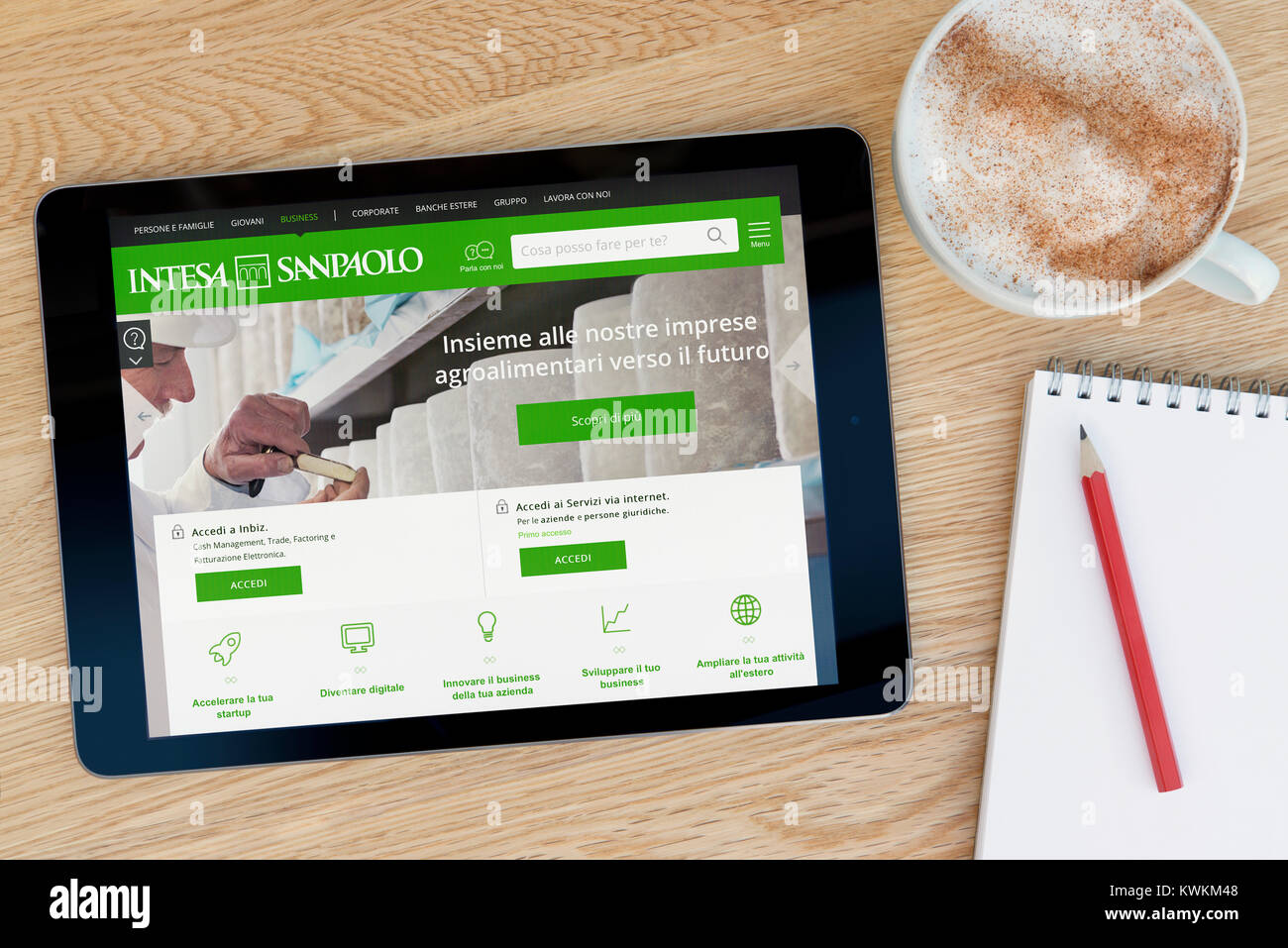 L'Intesa Sanpaolo site sur un iPad tablet device, reposant sur une table en bois à côté d'un bloc-notes, crayon et tasse de café (rédaction uniquement) Banque D'Images