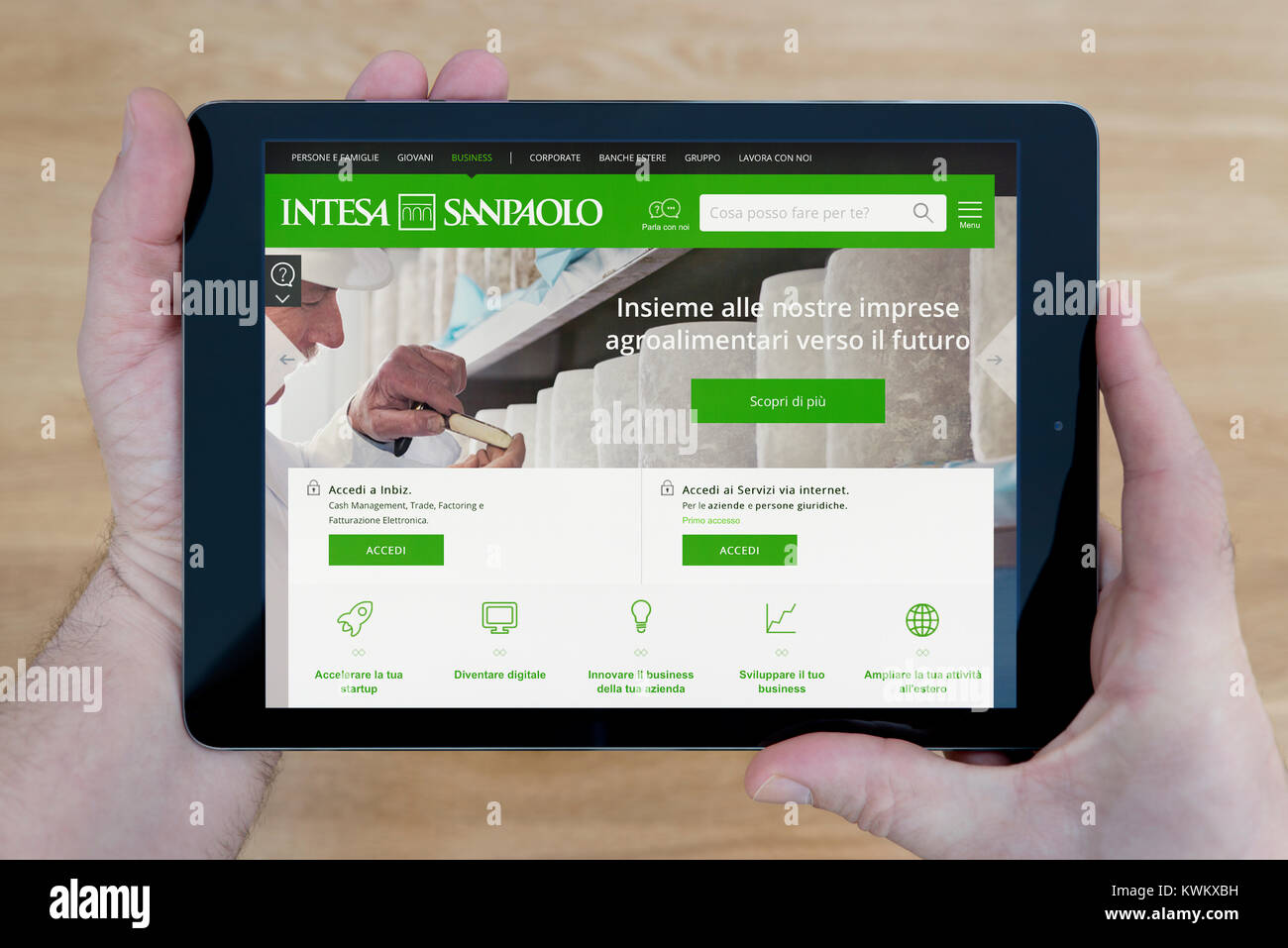 Un homme regarde le site web de la banque Intesa Sanpaolo sur son iPad tablet, sur une table en bois page contexte (usage éditorial uniquement) Banque D'Images