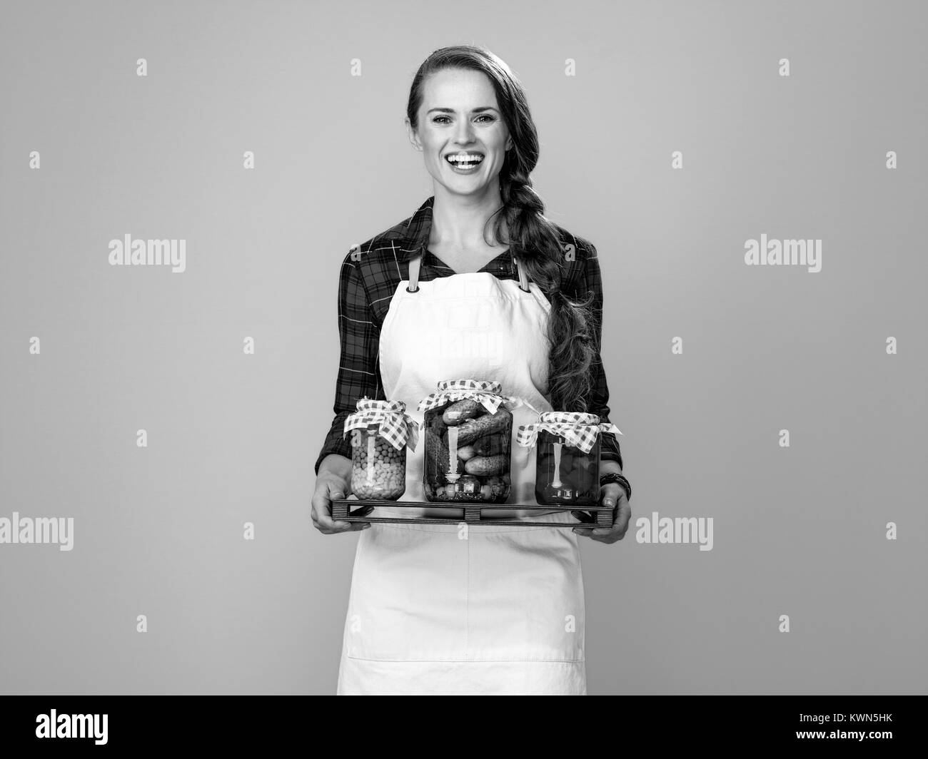 Des aliments sains à votre table. Portrait of happy young woman wearing apron cook isolé sur un jaune montrant des bocaux de légumes marinés Banque D'Images
