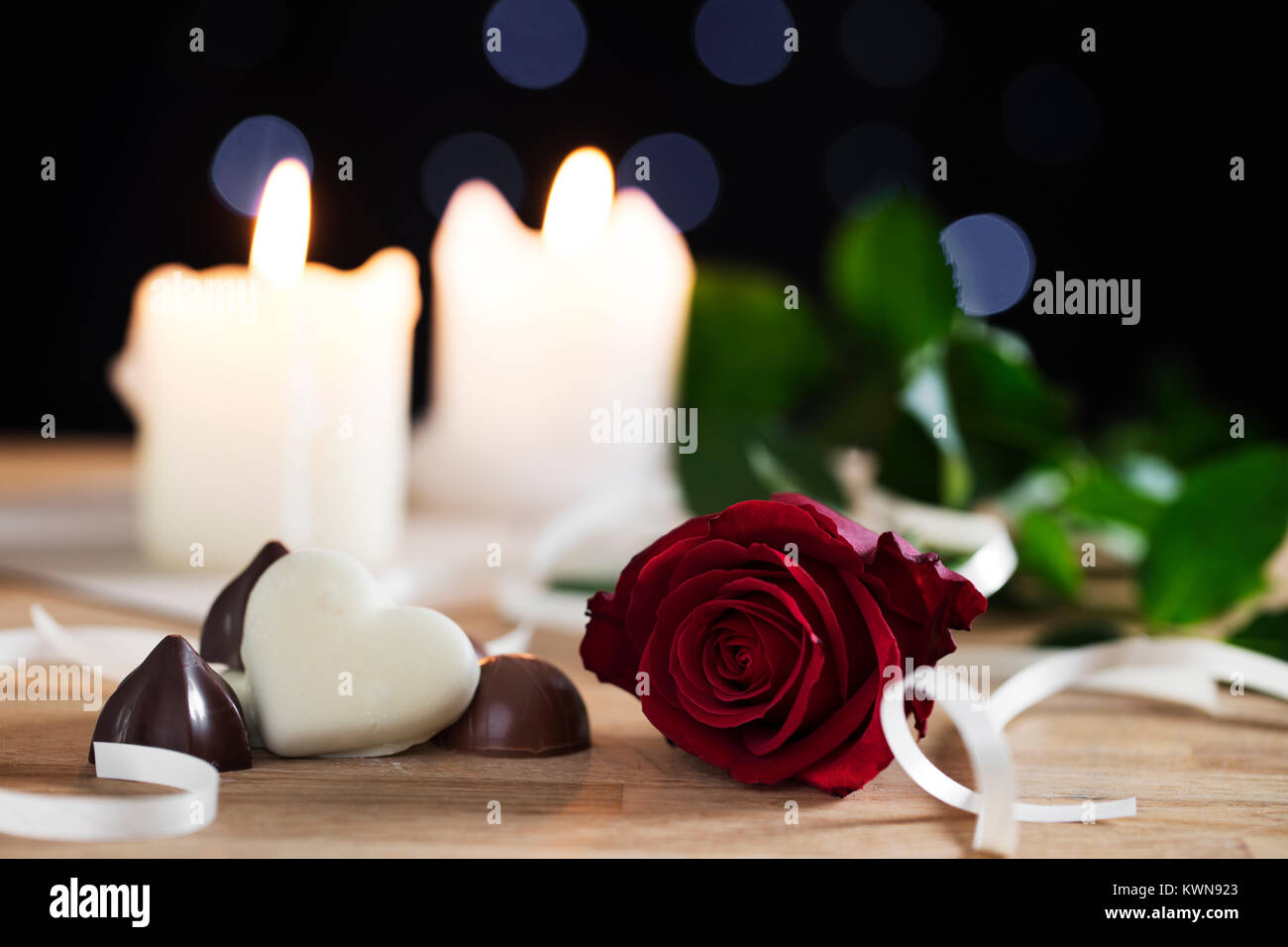 Rose rouge sur le tableau avec des chocolats et des bougies en arrière-plan, profondeur de champ. Banque D'Images