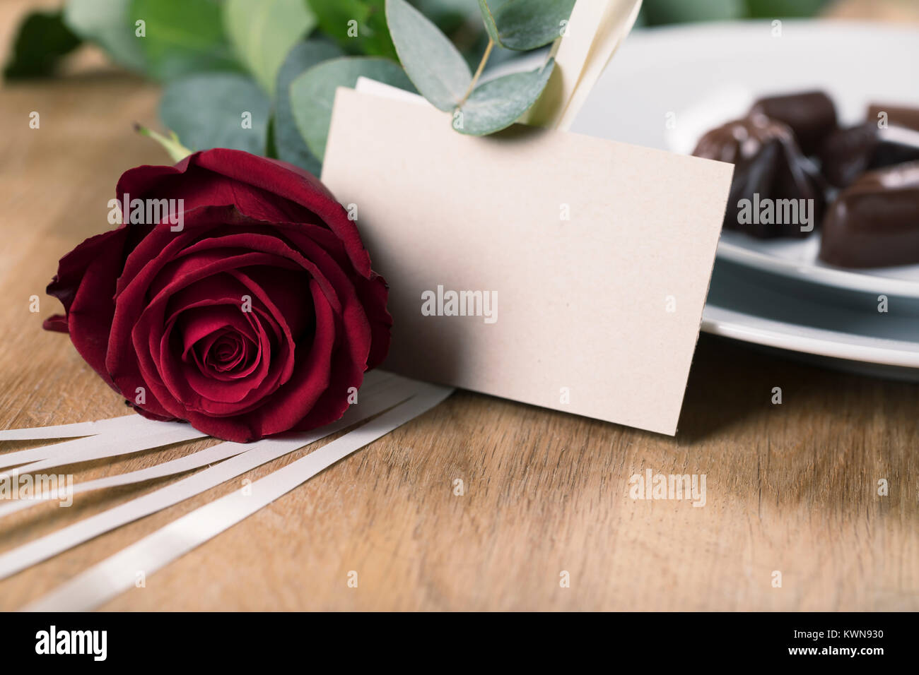 Close up of red rose et carte vierge avec la plaque de chocolats dans l'arrière-plan Banque D'Images