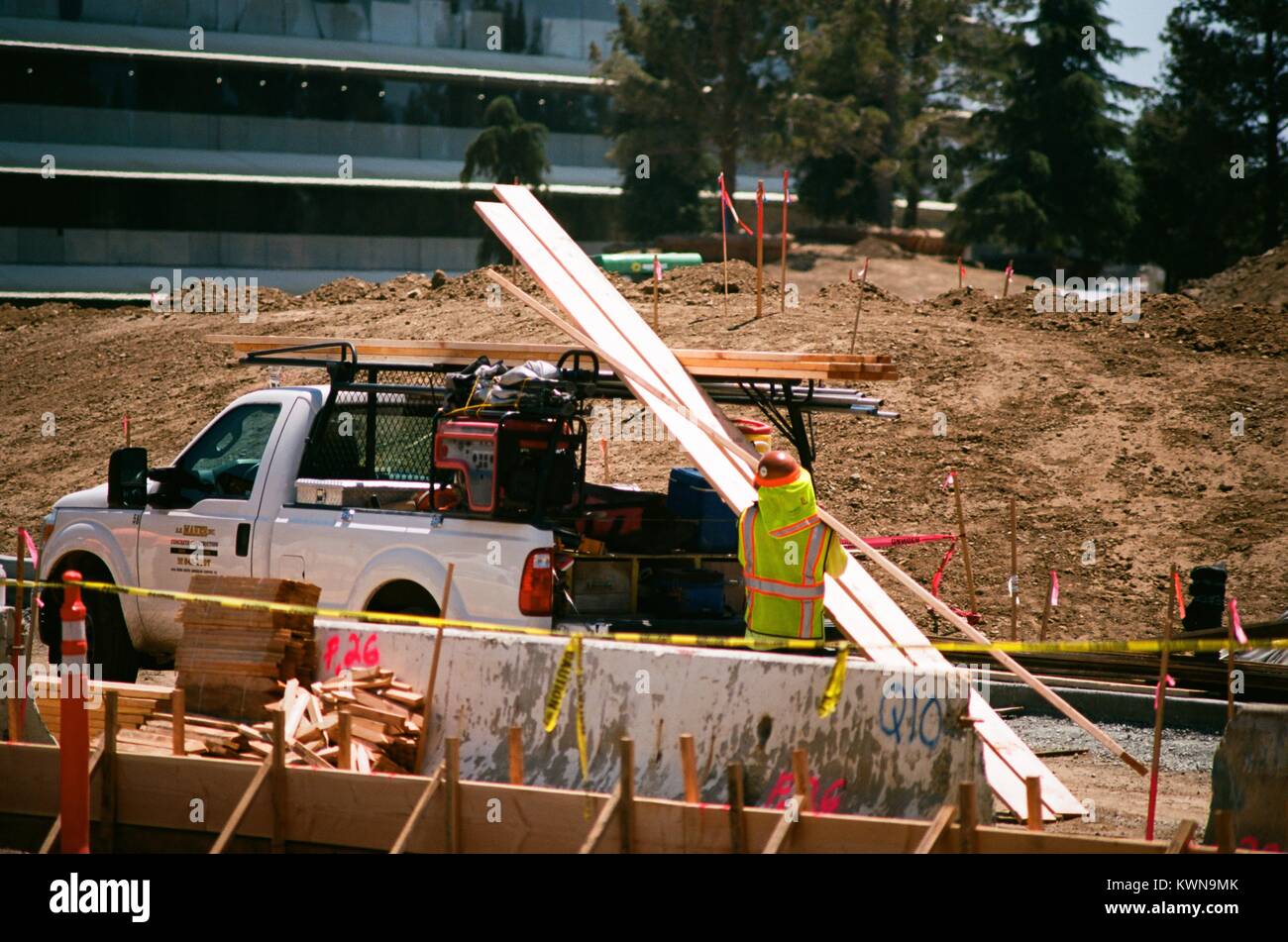 Libre d'un travailleur de la construction avec un gilet de chargement des matériaux de construction sur une camionnette, avec partie de l'immeuble principal, visible à l'Apple Park, connu familièrement comme "le vaisseau spatial", le nouveau quartier général d'Apple Inc dans la Silicon Valley ville de Cupertino, Californie, 25 juillet 2017. Banque D'Images