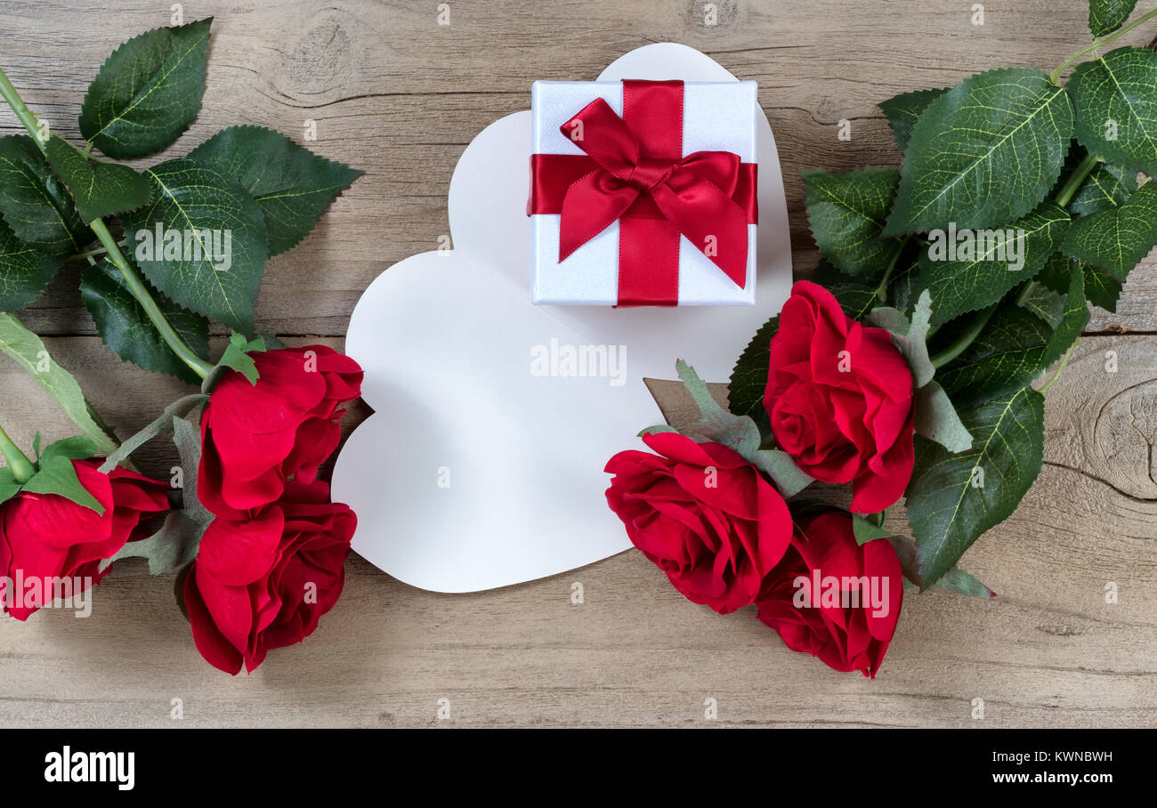 Roses rouges entourant boîte cadeau blanche sur fond de bois patiné en vue mise à plat Banque D'Images