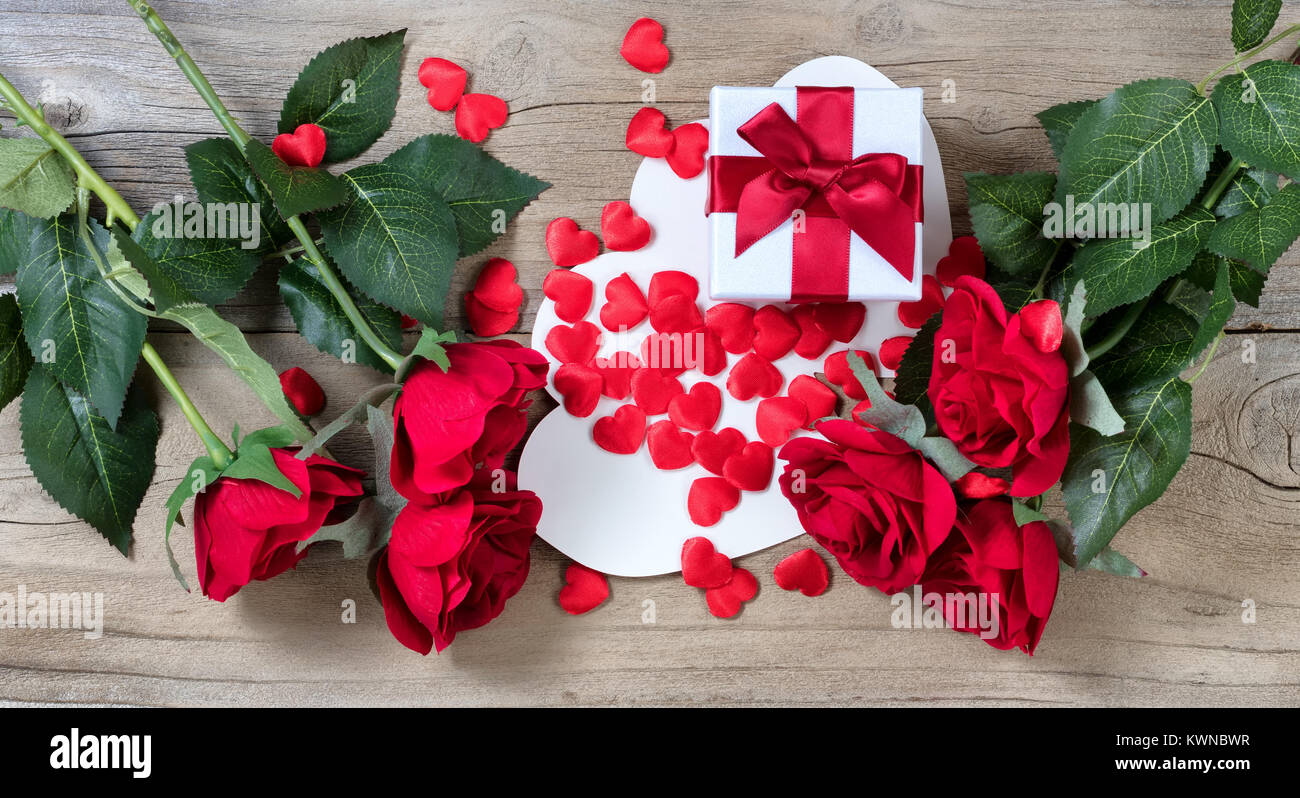 Roses rouges entourant white boîte cadeau et beaucoup de cœurs sur fond de bois patiné en vue mise à plat Banque D'Images