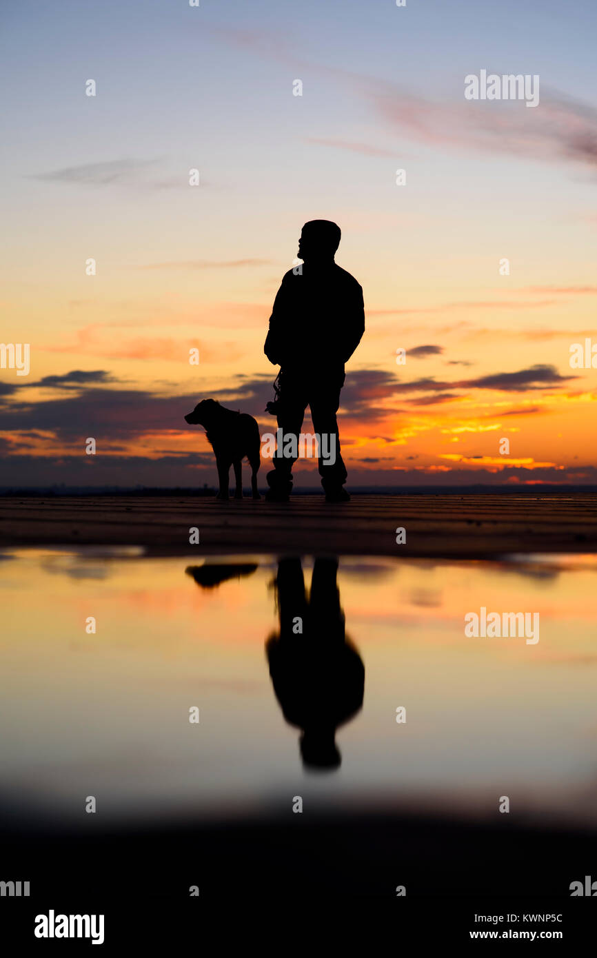 Silhouette d'homme avec son chien au coucher du soleil sur l'arrière-plan Banque D'Images