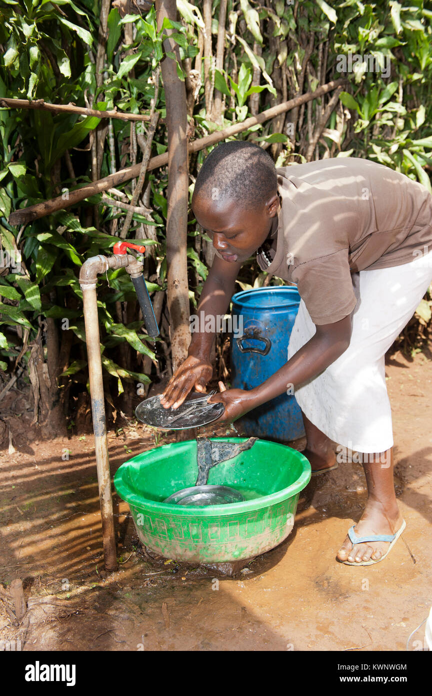 Girl lave-ustensiles de cuisine dans un bol d'eau, au Rwanda. Banque D'Images