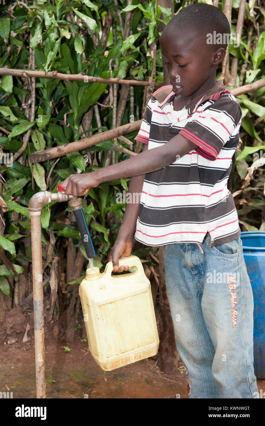 La collecte d'un enfant rwandais de contenant de l'eau d'un tuyau de support. Banque D'Images