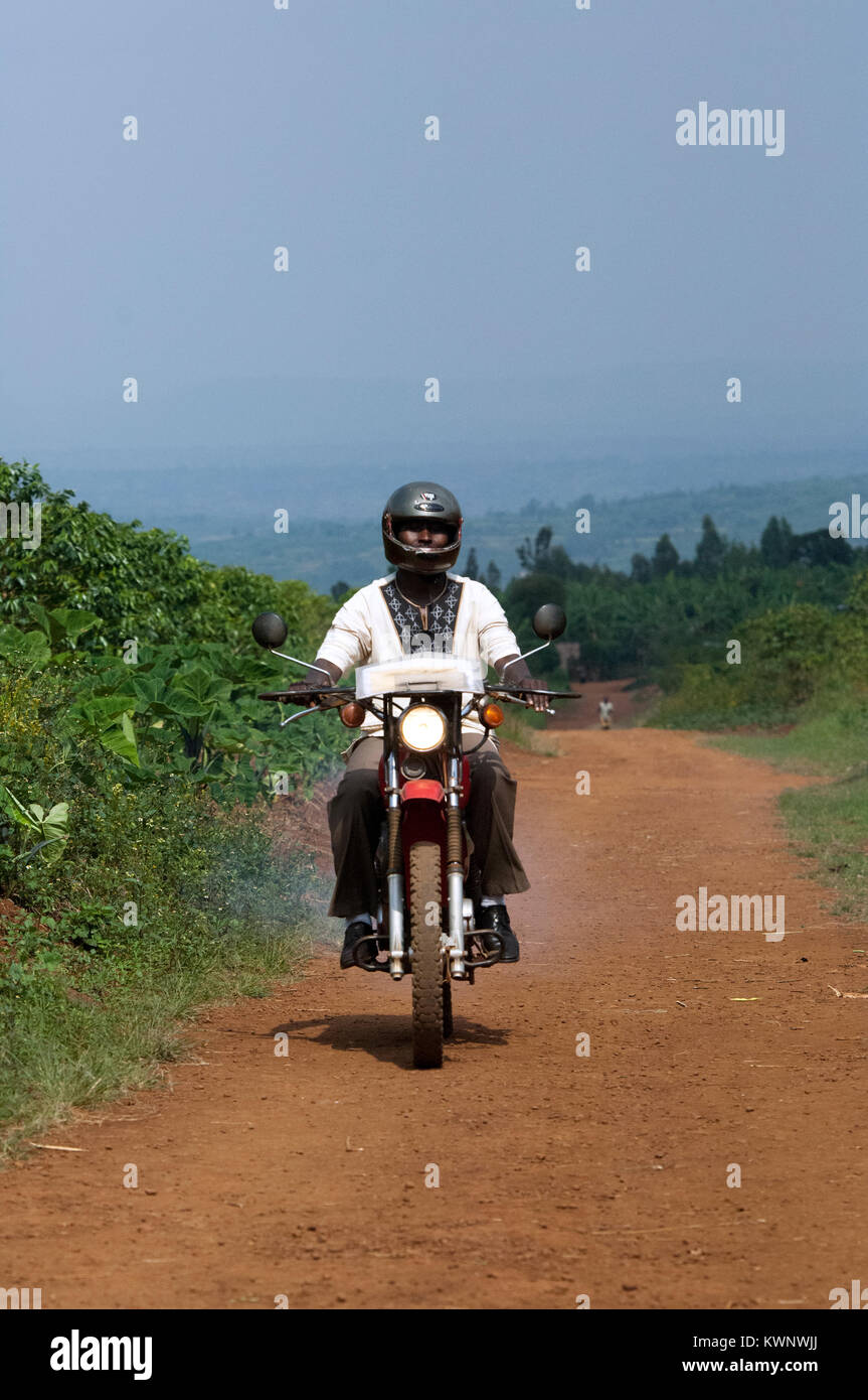 Travailleur de l'aide de bienfaisance sur une moto passe le long d'une piste poussiéreuse, le Rwanda. Banque D'Images