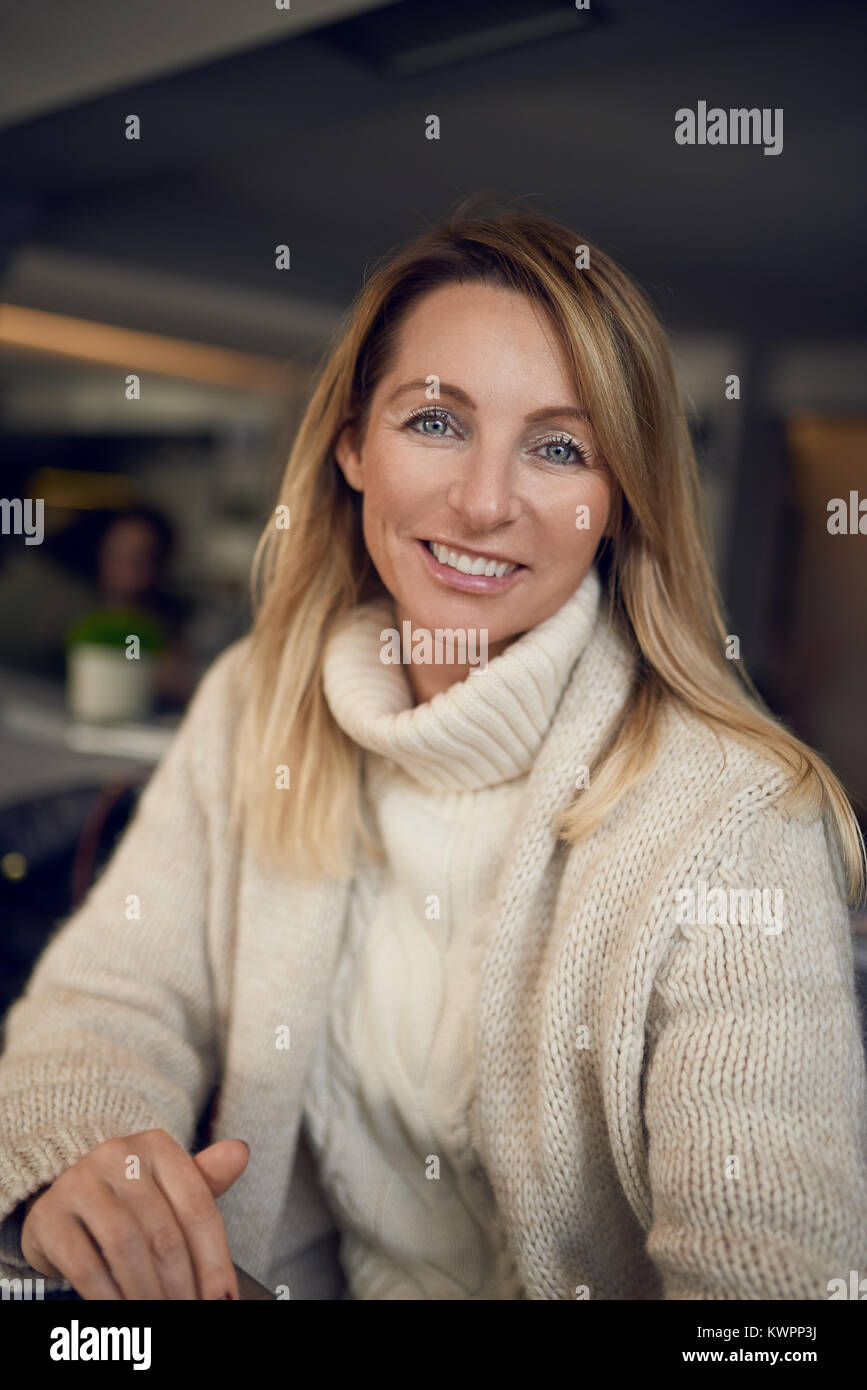 Attractive blonde woman smiling at the camera tout en appréciant un verre de vin à l'intérieur à un pub ou restaurant Banque D'Images
