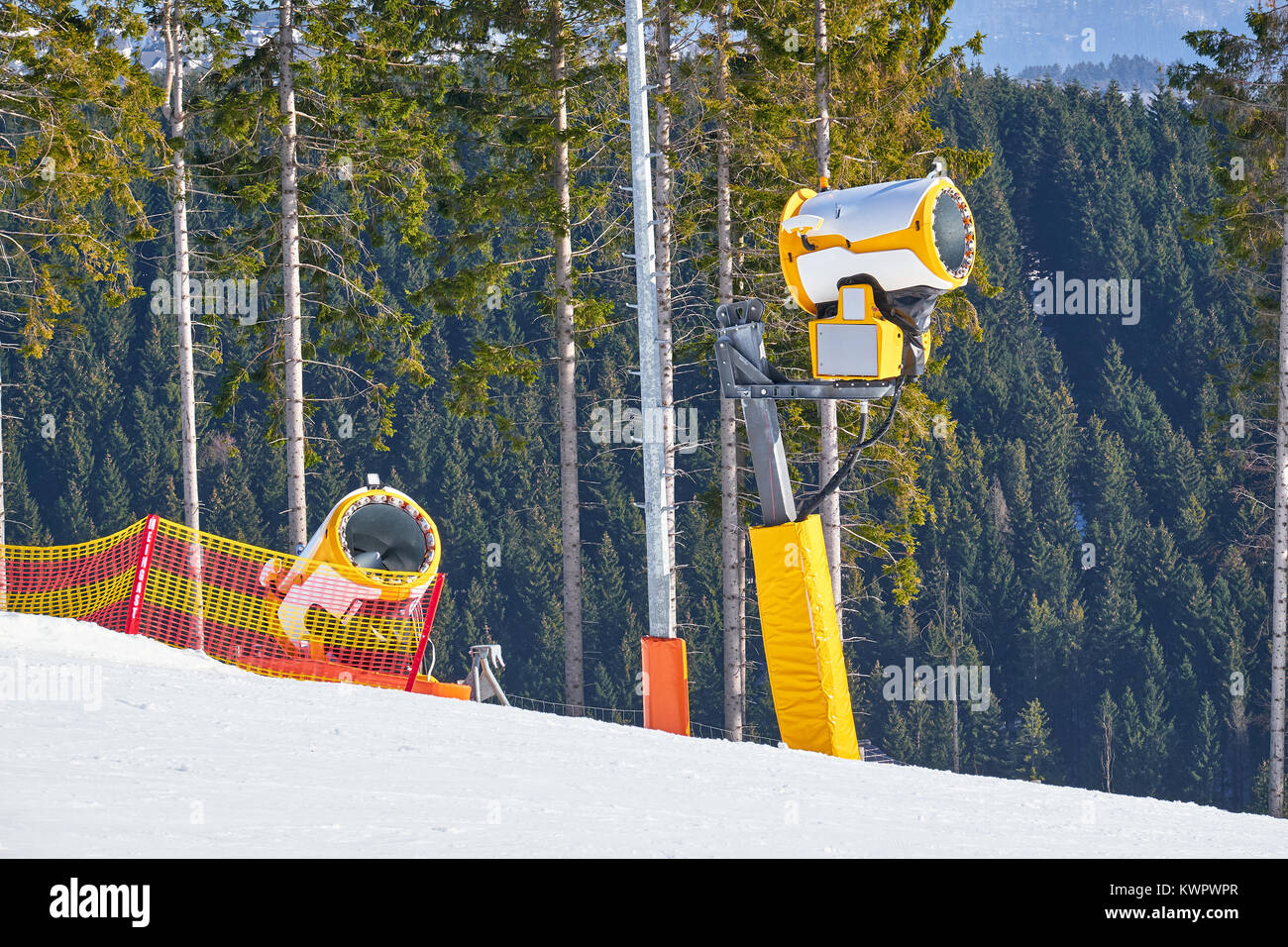 Deux canons à neige jaune éteint sur une piste de ski de Winterberg carrousel avec forêt de pins à l'arrière-plan Banque D'Images