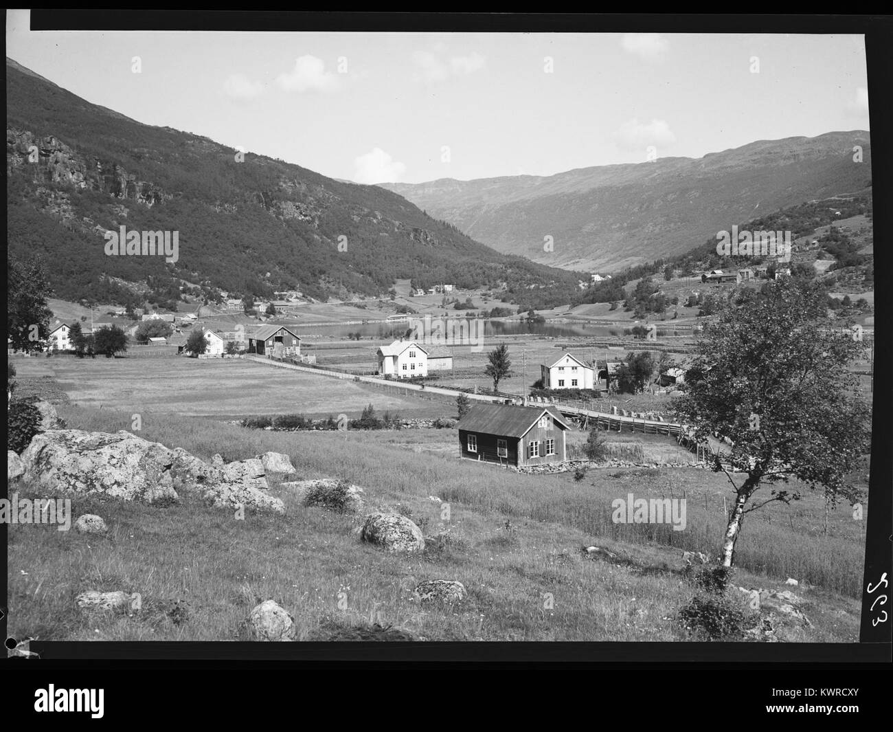 La photographie en noir et blanc de 2015 de Øye à Valdres, en Norvège, présente une scène de village au bord du lac avec des maisons en bois groupées, une ligne d'arbres le long du rivage, des montagnes lointaines et des eaux tranquilles du lac Vangsmjøse, illustrant l'établissement et le paysage dans le district. Banque D'Images
