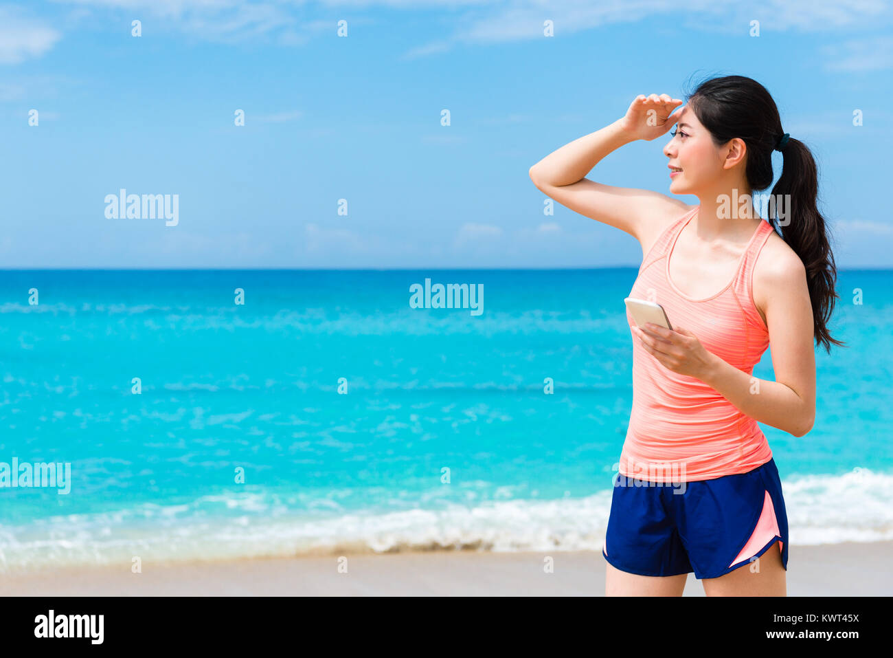 Jolie remise en forme élégante woman standing on beach en utilisant mobile cell phone recherchant l'information locale et à billet paysage. Banque D'Images