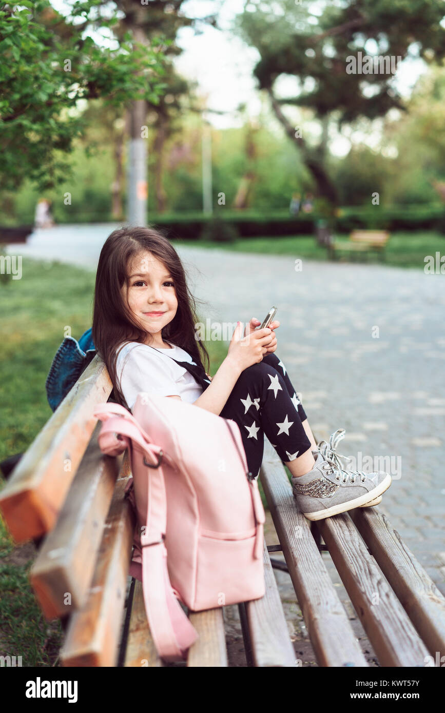 Petite fille avec un smartphone assis sur un banc Banque D'Images
