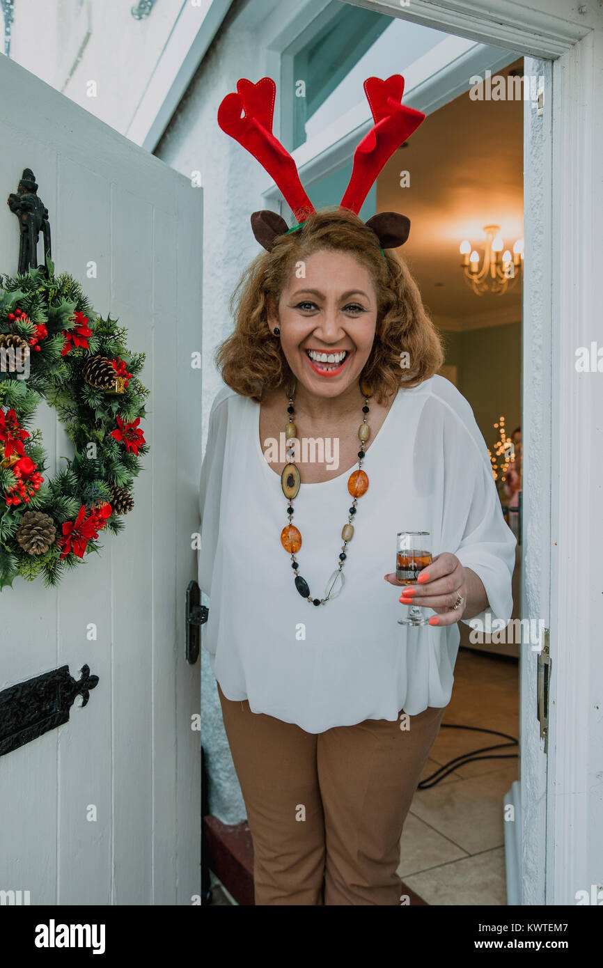 Point de vue de la cheerful senior femme pour vous accueillir dans sa maison pour Noël. Elle porte les bois et tenant un verre de porto. Banque D'Images