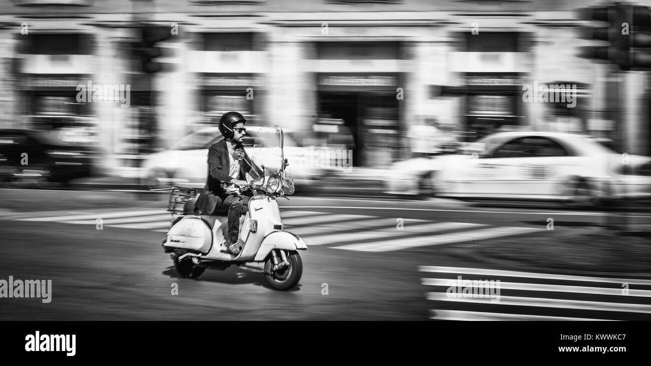 Jeune homme monté sur une moto dans la rue de la ville de Rome, Italie. Capturé en monochrome et en mouvement. Banque D'Images