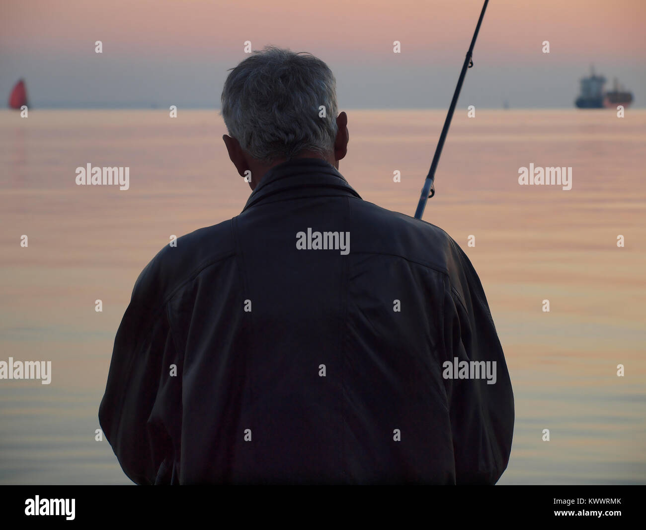 Silhouette d'un homme avec une canne à pêche au coucher du soleil Banque D'Images