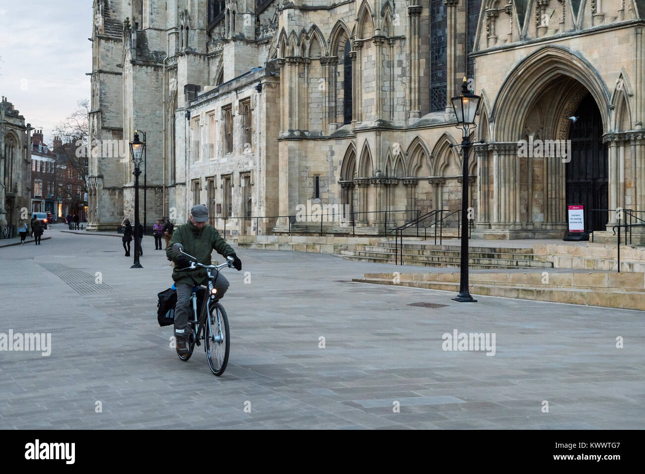 Centre de New York - un homme âgé le vélo, cycles à travers la piazza, passé l'entrée de la magnifique cathédrale de York - North Yorkshire, Angleterre, Royaume-Uni. Banque D'Images