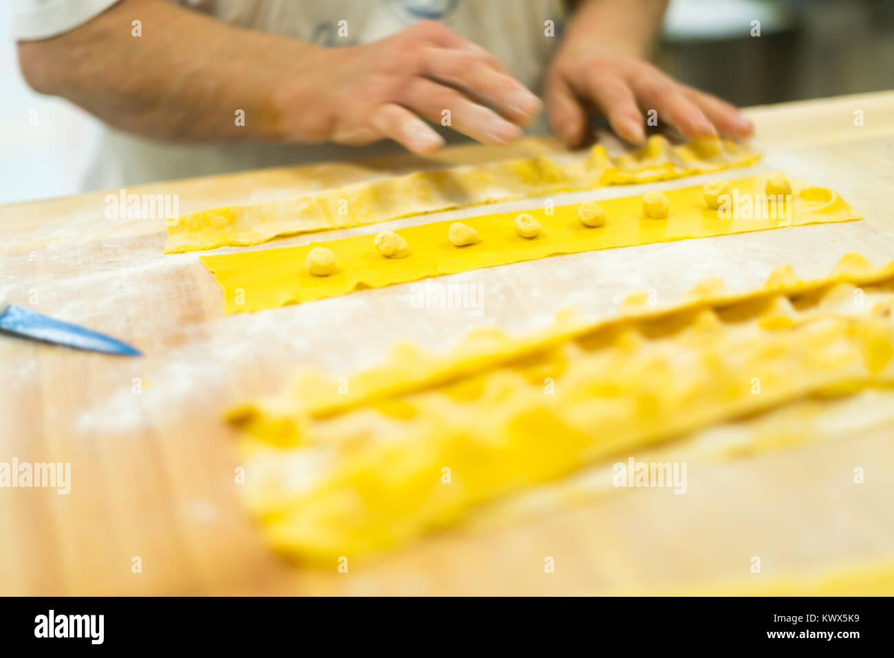 Caucasien italien années 70 80 dame âgée avec des mains ridées préparant des tortelli et d'autres pâtes farcies dans la cuisine de la boulangerie. Banque D'Images