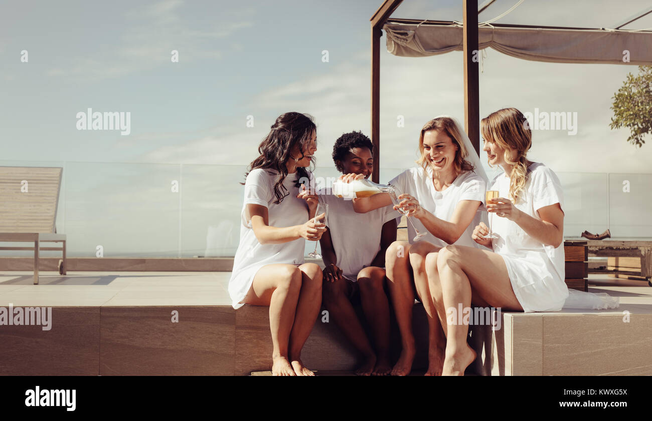 Jeune mariée joyeuse pouring champagne dans les verres. Mariée et demoiselles d'avoir une partie de bachelorette sur toit. Banque D'Images