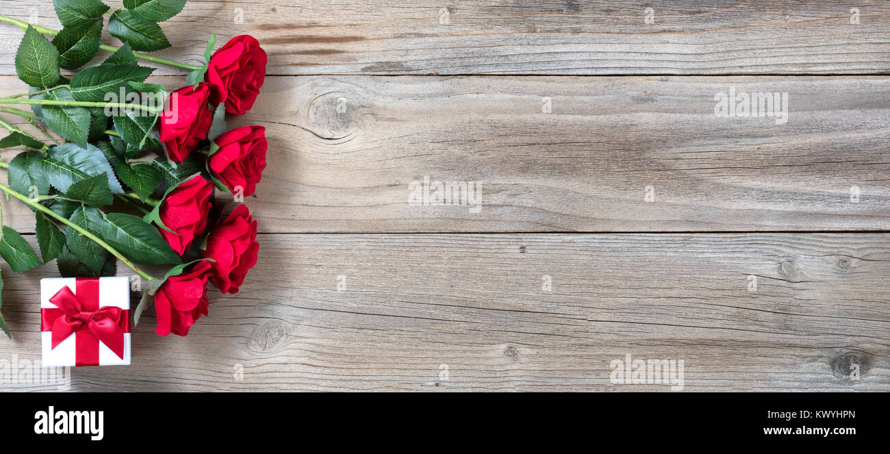 Demi-douzaine de roses rouges et boîte-cadeau à gauche de la télévision en bois rustique vue laïcs Banque D'Images