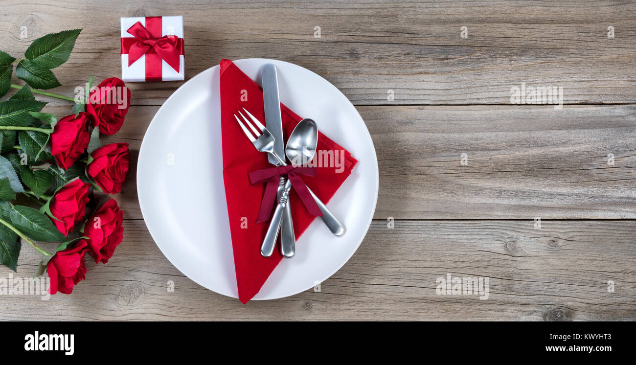 Le dîner de la Saint-Valentin avec une demi-douzaine de roses rouges et de l'argenterie sur bois rustique en vue mise à plat Banque D'Images