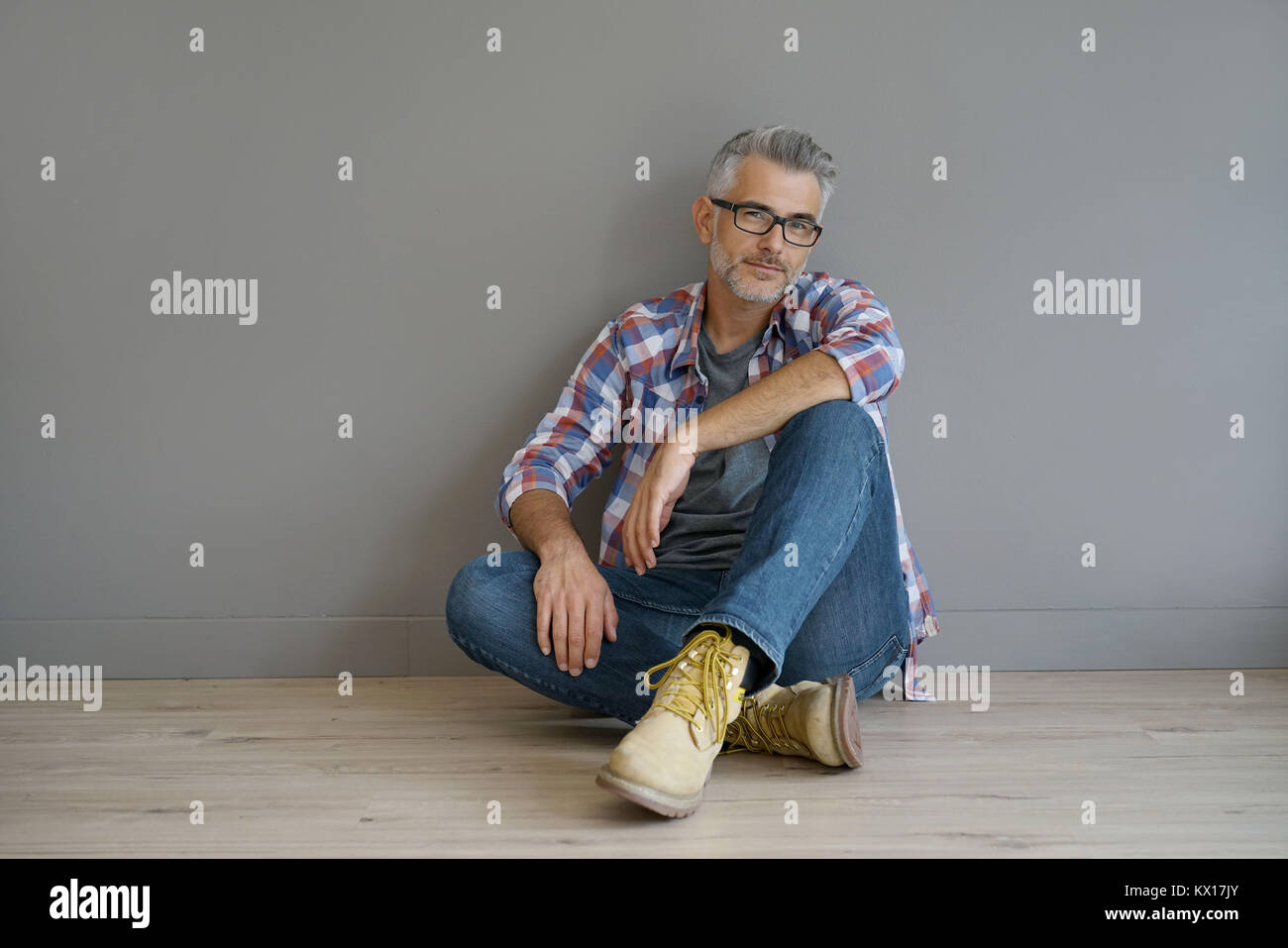 Trendy homme de 40 ans assis sur le plancher, isolé Banque D'Images