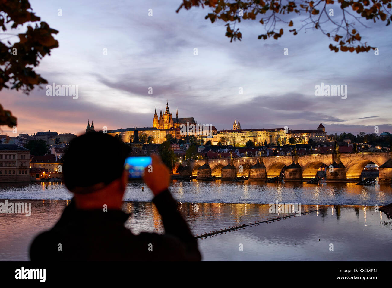 Vue sur le château de Prague dans la lumière du soir vue sur la Vltava, à partir de la rive du fleuve ; prendre des photos touristiques avec téléphone appareil photo en premier plan Banque D'Images