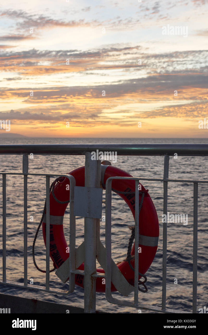 Une bouée orange vif la vie anneau attaché à la rambarde d'un navire de passage entre les îles Philippines au coucher du soleil. Banque D'Images