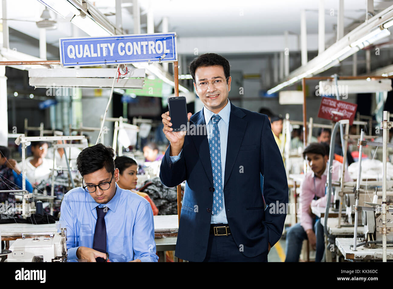 1 Homme Factory-Owner talking On Mobile-phone et WorkersTailors Travailler Banque D'Images