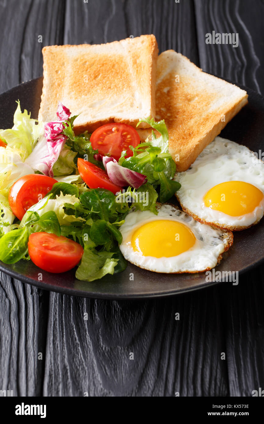 Petit déjeuner copieux : oeufs au plat avec une salade de légumes frais et de pain grillé sur une plaque verticale. Banque D'Images
