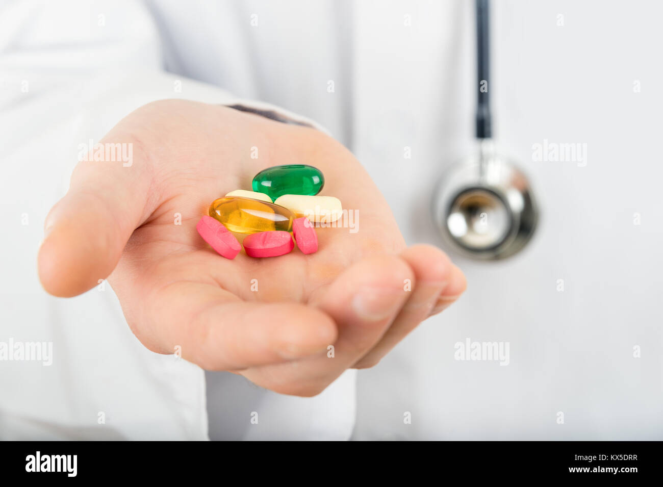 Plusieurs médicaments différents comprimés dans la main d'un médecin détenant un stéthoscope Banque D'Images